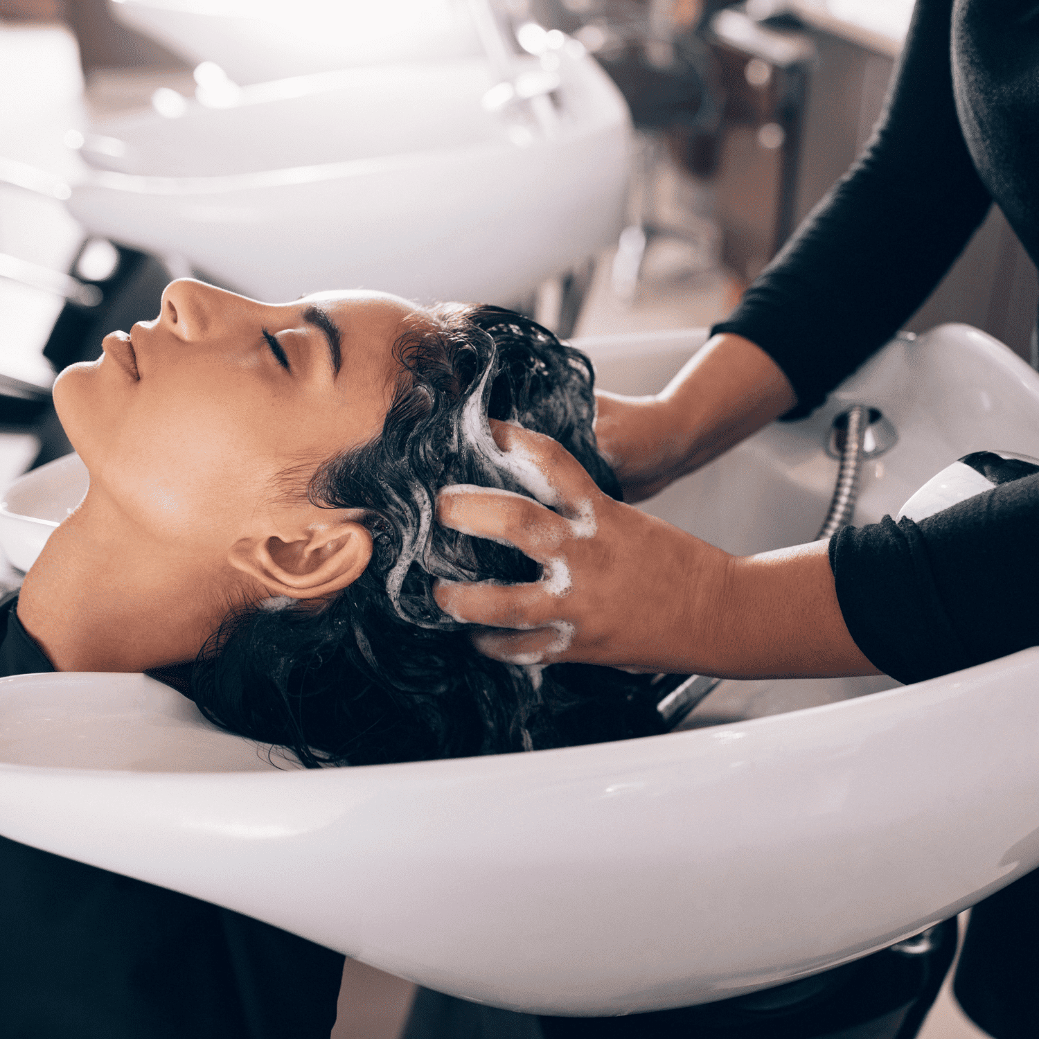 Person getting hair washed at a salon sink by a stylist with foamy shampoo.